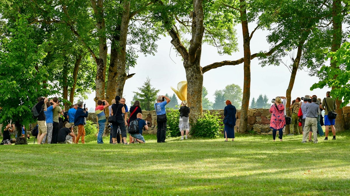 A large group of photographers with cameras taking pictures together during an outdoor photography workshop in a green park.