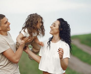 A joyful family moment outdoors with parents playing with their daughter.