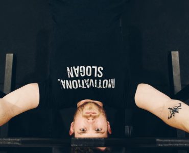 Bearded sportsman in t shirt with inscription exercising with weight while looking at camera