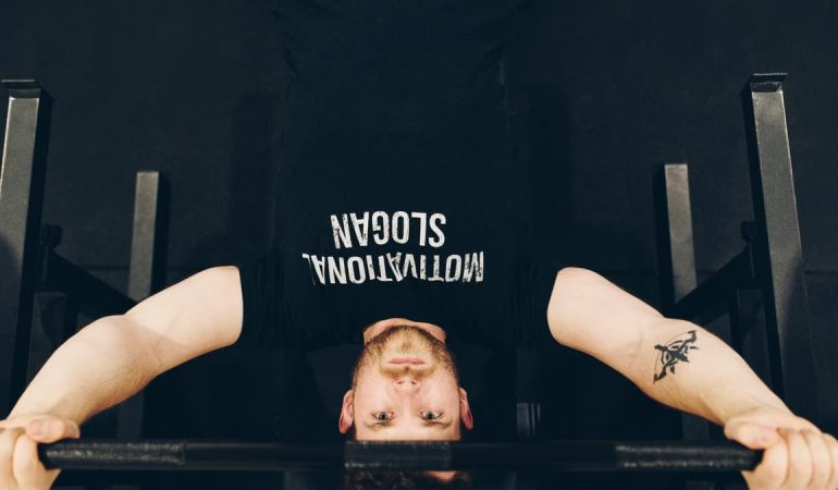 Bearded sportsman in t shirt with inscription exercising with weight while looking at camera